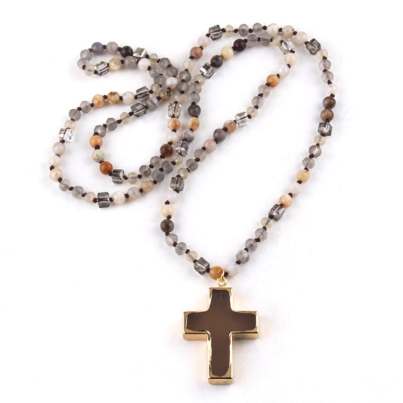 a gold-toned cross pendant with a dark brown inlay hangs from a bohemian natural stone and glass beaded necklace featuring mixed earthy tones of gray beige and orange beads with clear crystal accents