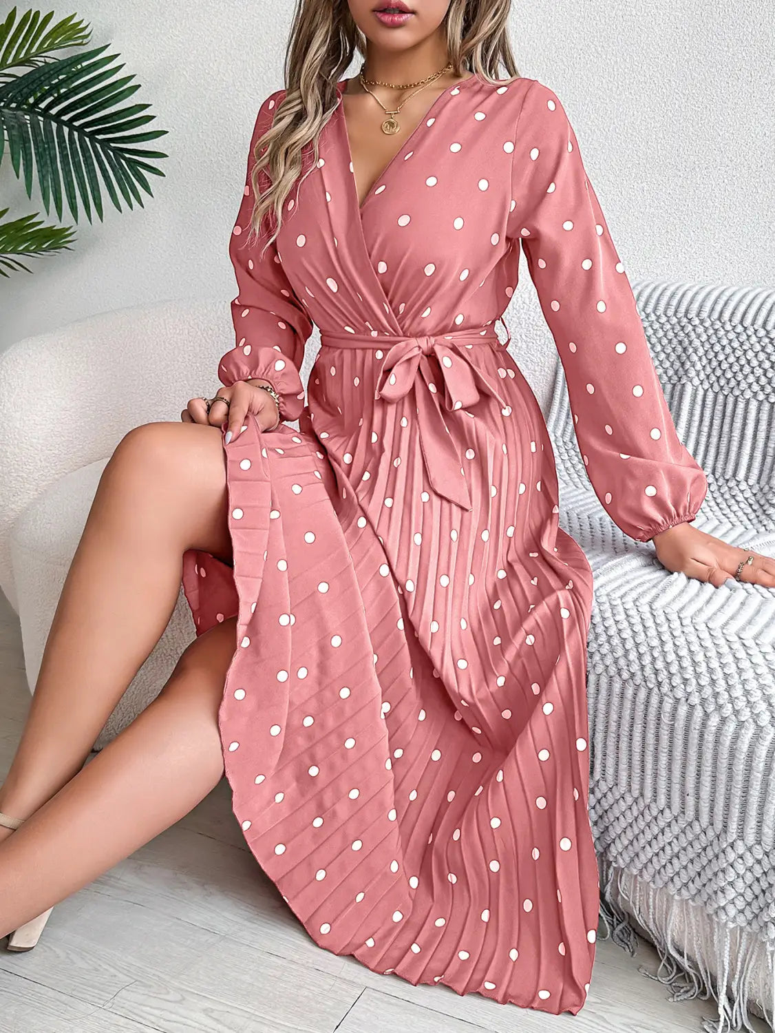 a flowing pink polka dot pleated maxi dress with long sleeves and a self-tie belt featuring a v neck design