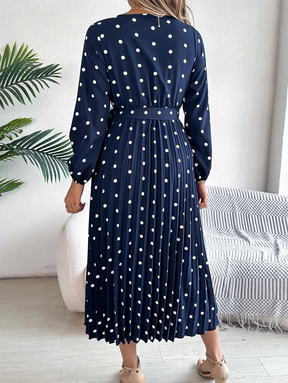 a navy blue polka dot midi dress with white dots featuring long sleeves and a pleated skirt in a v neck design