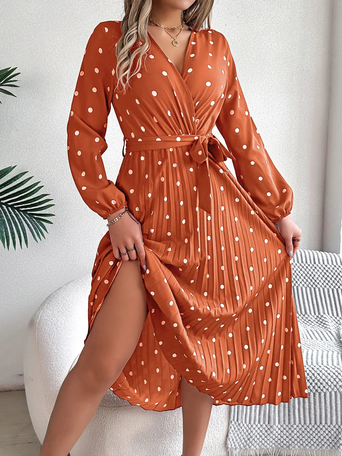 A flowing orange polka dot pleated v neck long sleeve maxi dress with white dots and a self-tie belt.