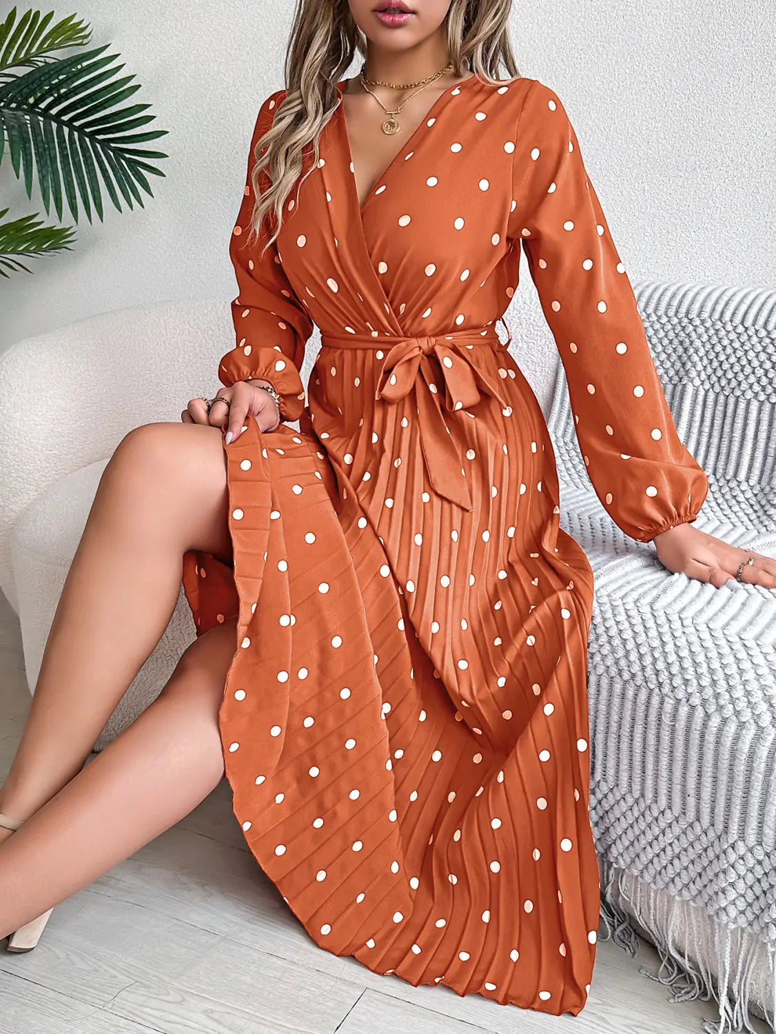A flowing rust-colored polka dot pleated v neck long sleeve maxi dress with a self-tie belt and white dots.