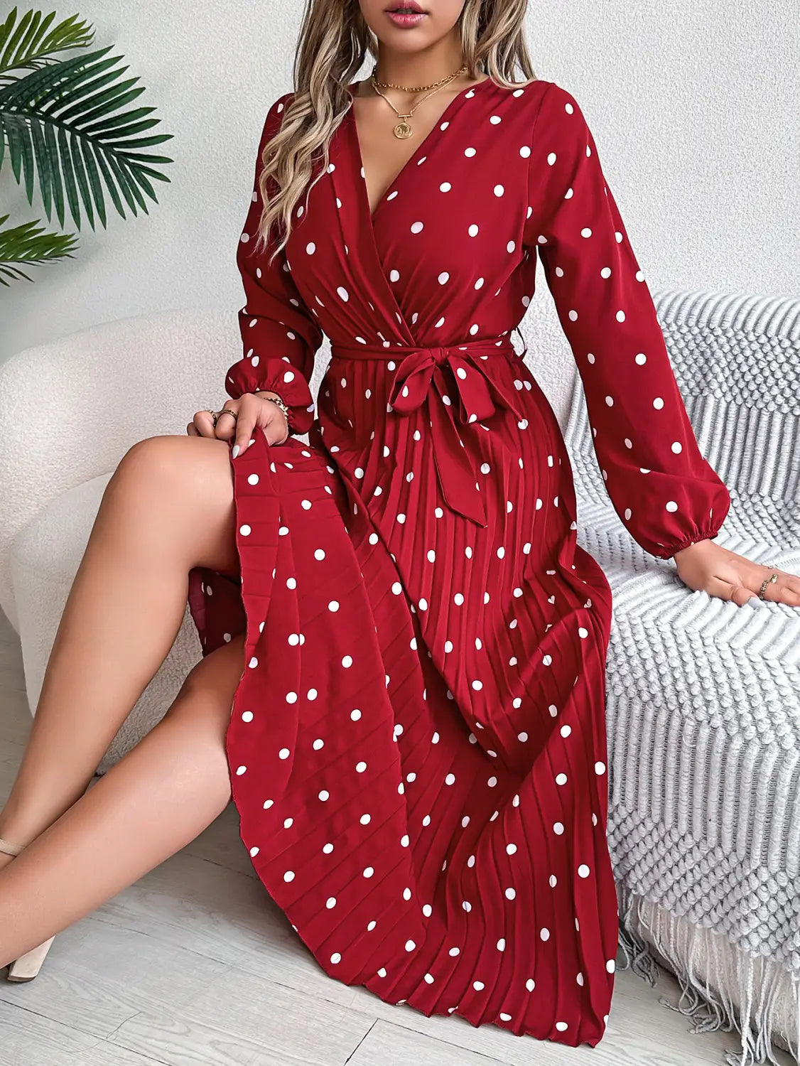 A red polka dot pleated v neck long sleeve maxi dress with a wrap design and a flowing skirt.