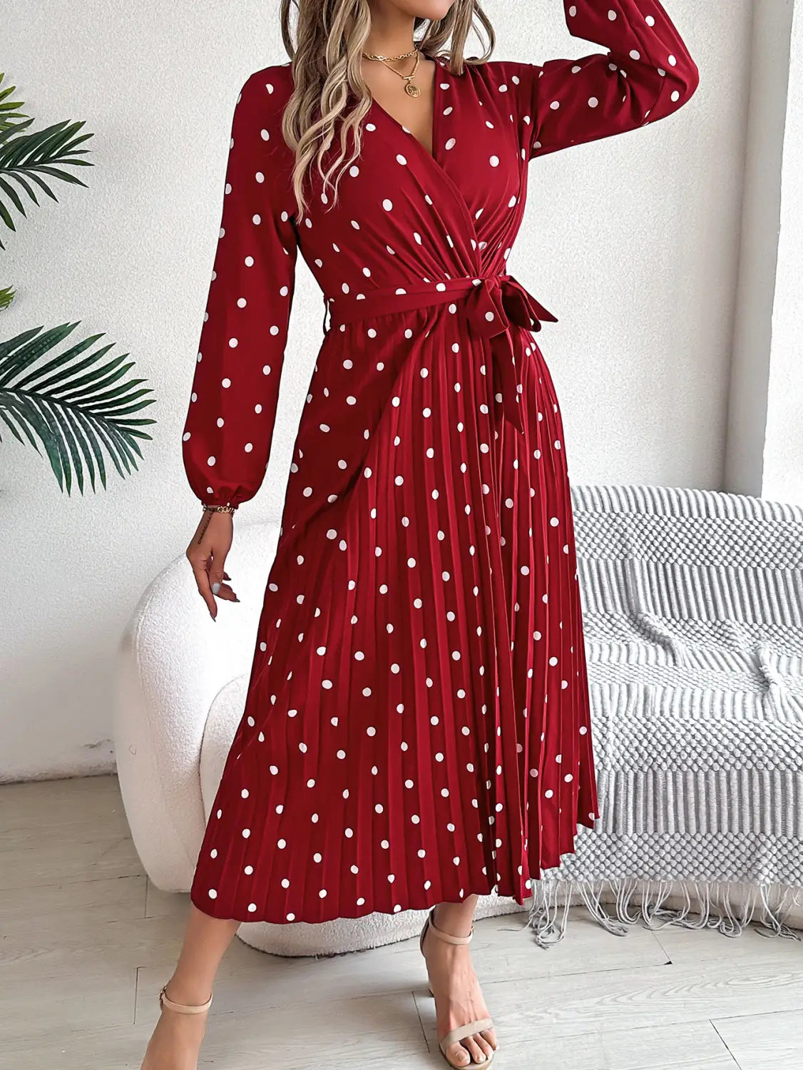 A red polka dot maxi dress with a pleated skirt, long sleeves, a v neck, and a self-tie belt.