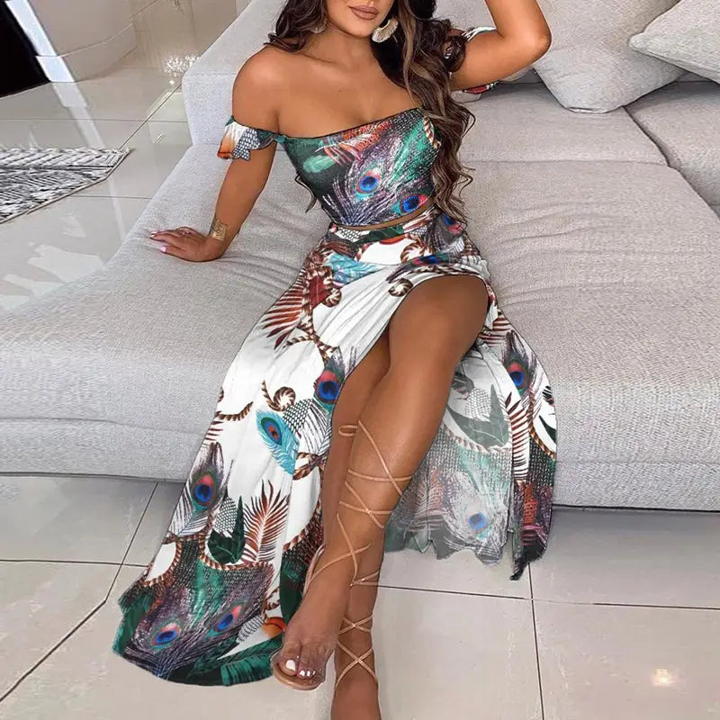 A vibrant peacock feather print bohemian off-shoulder two-piece maxi dress with a crop top and high-slit skirt in white green blue and brown tones.
