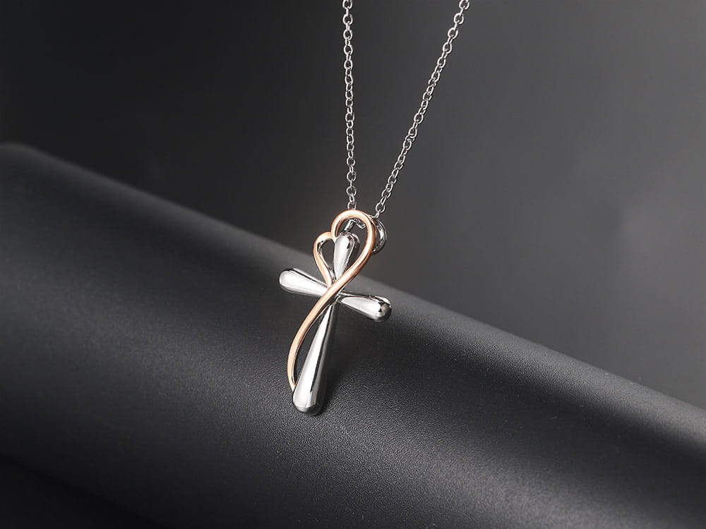 A two tone silver and rose gold heart infinity cross pendant hanging from a delicate chain, showcasing a blend of metals in a stylish necklace.