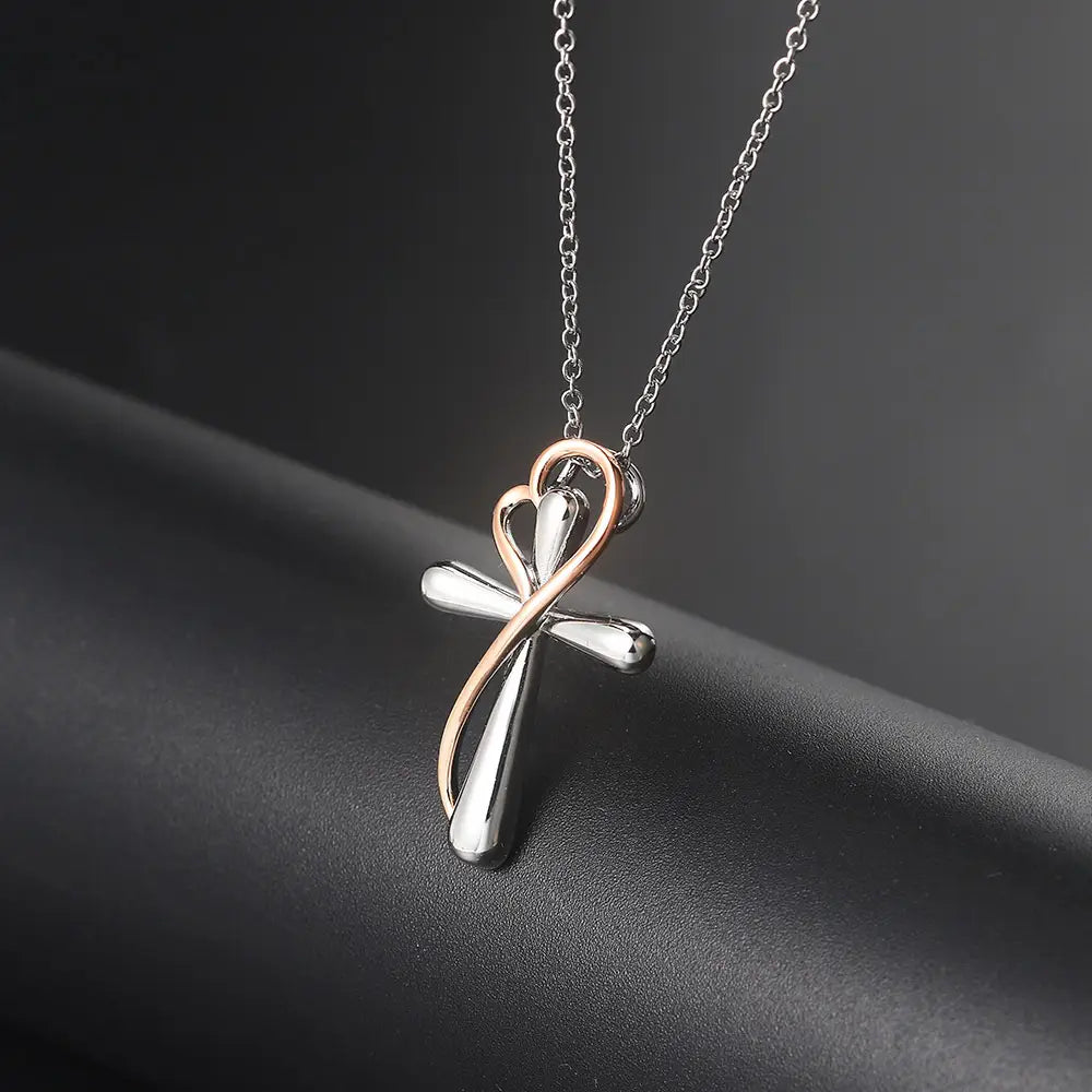 A delicate two tone silver and rose gold cross pendant necklace featuring a sleek design with an elegant intertwined heart motif.
