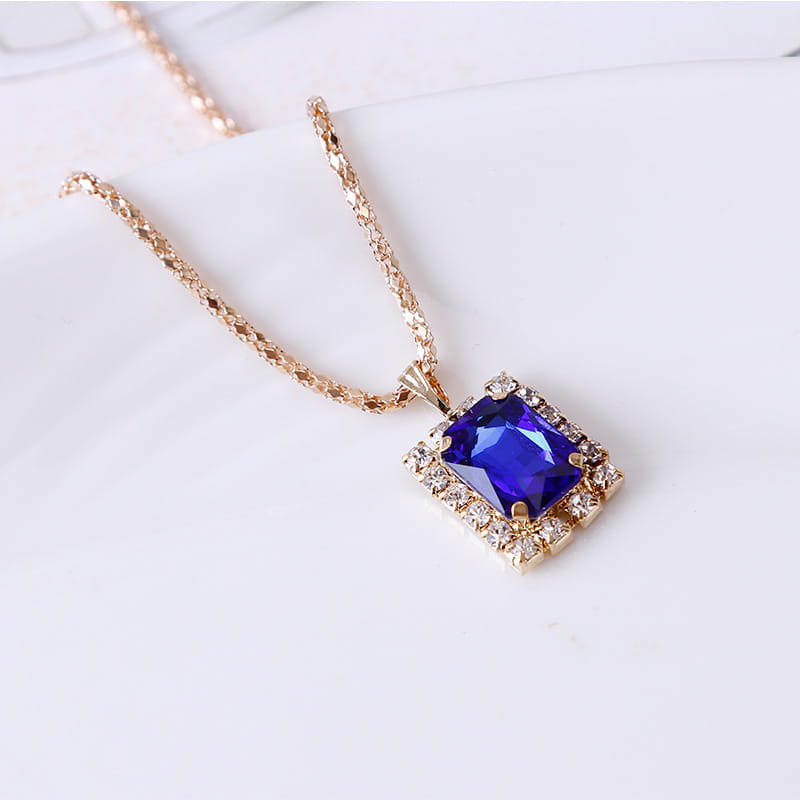 Elegant rectangular gemstone gold jewelry three piece set featuring a gold-toned necklace with a square pendant showcasing a deep blue gemstone surrounded by smaller clear crystals.