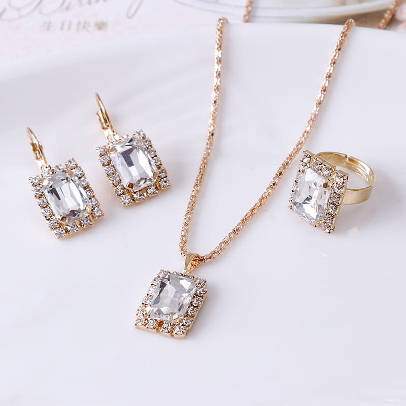Elegant rectangular gemstone gold jewelry three piece set featuring gold-toned delicate chain necklace and matching earrings with clear rectangular crystal stones surrounded by smaller rhinestones.