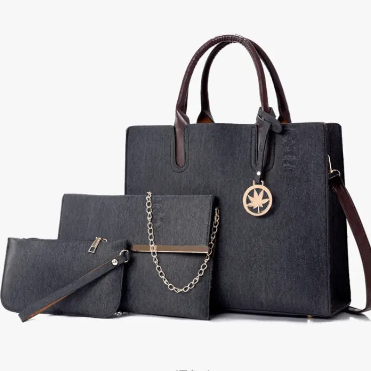 dark gray textured handbag with brown leather handles and gold maple leaf charm from the denim and leather three piece multi compartment handbag set