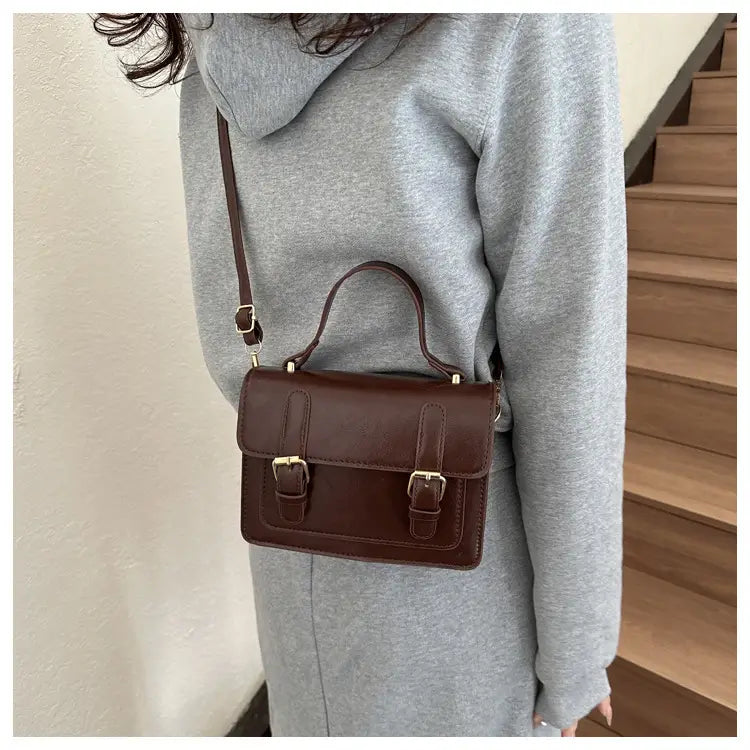 Sacoche vintage en cuir brun à effet cuir synthétique, avec boucles en ton or et anse supérieure.