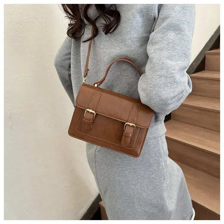 Sacoche en cuir brun avec deux boucles en ton or et une anse supérieure, dans une sacoche vintage en effet cuir synthétique à boucles dorées produit.