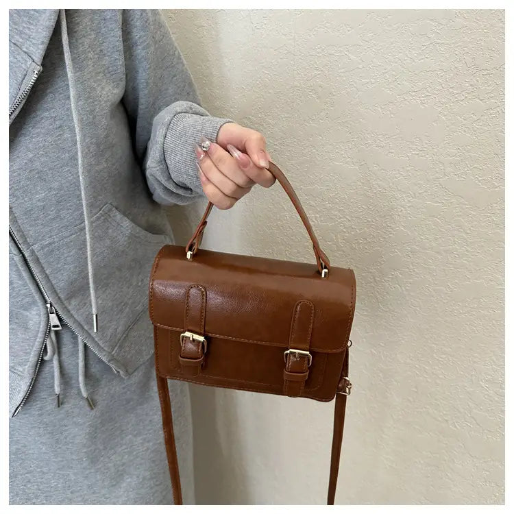Sacoche vintage en cuir brun à effet cuir synthétique, avec deux boucles avant dorées et une anse supérieure pour un port polyvalent.