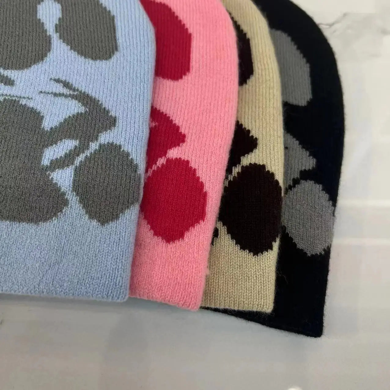 A collection of knitted letter jacquard beanie warm winter hats in pastel and dark tones featuring bold abstract floral patterns with contrasting circular motifs.