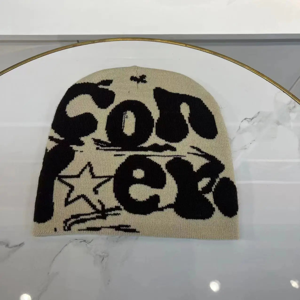 Beige knitted letter jacquard beanie featuring bold black conex lettering and a star graphic designed as a warm winter hat.