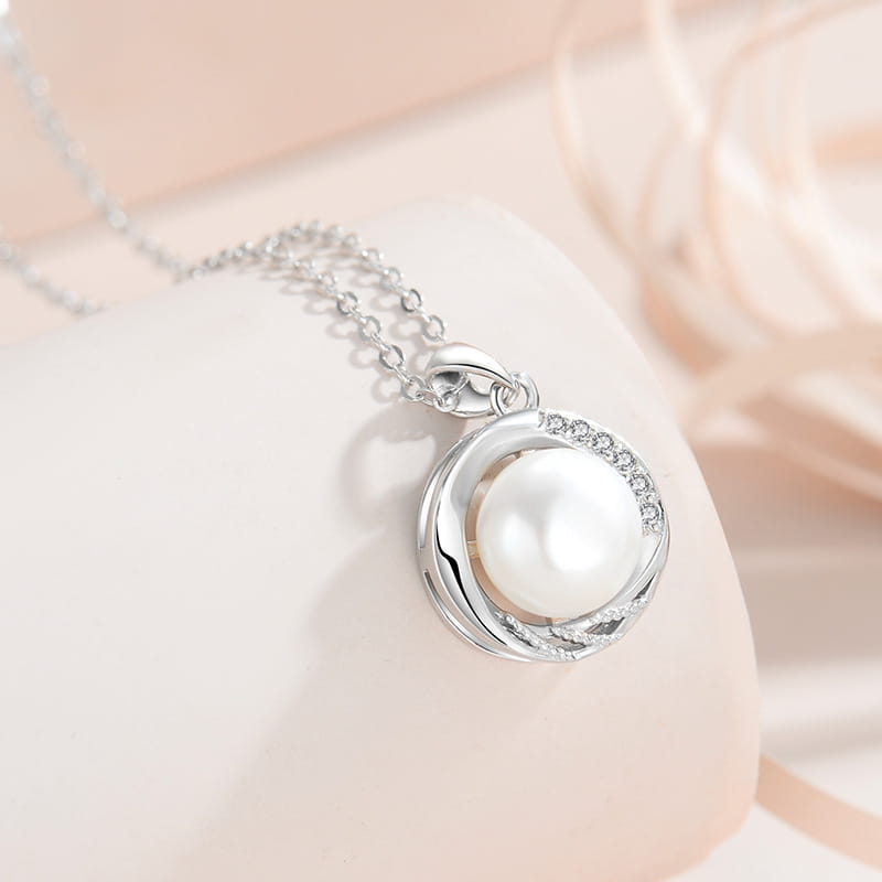 Sterling silver round freshwater pearl pendant necklace with a central white pearl encircled by delicate swirling metalwork and small sparkling diamonds set along the edge.