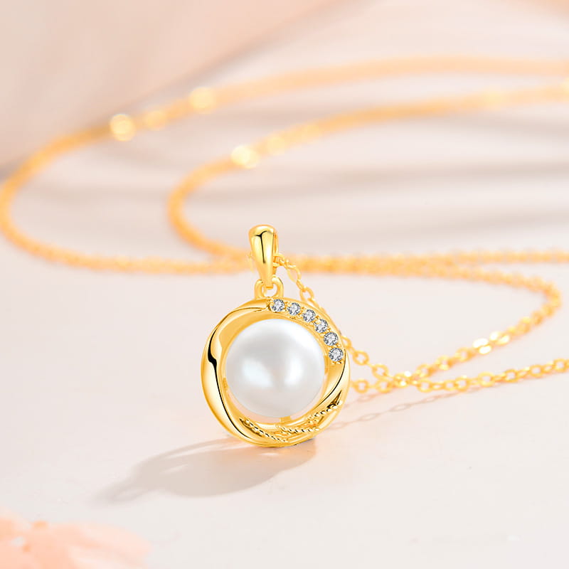 Sterling silver round freshwater pearl pendant necklace featuring a central white pearl encircled by an ornate gold band accented with small clear stones.