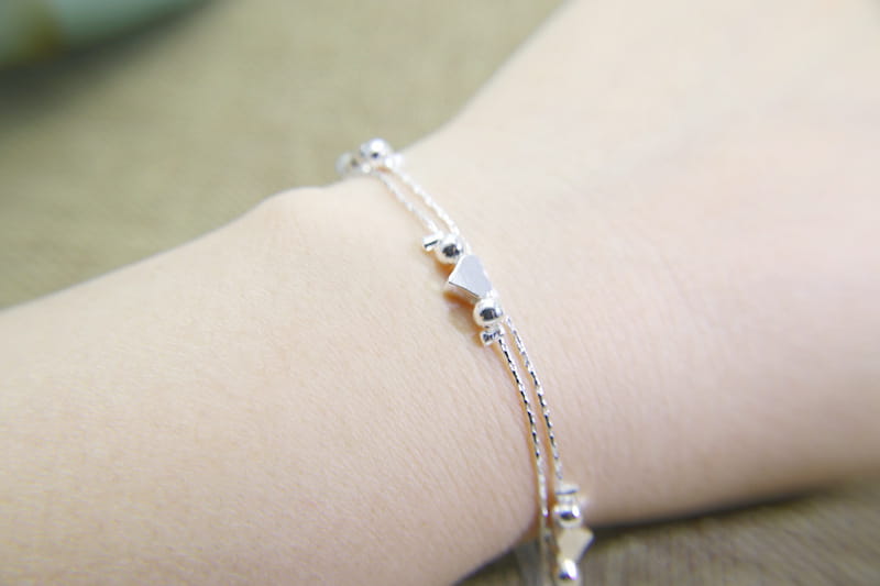 A delicate Korean double layer silver heart bead bracelet featuring a silver chain with small spherical beads and a central triangular charm.