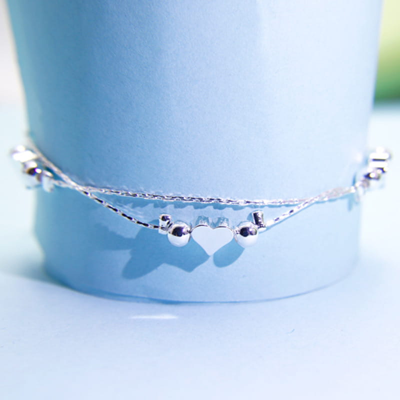 A delicate korean double layer silver heart bead bracelet featuring a central heart charm flanked by small spherical beads connected to fine silver chains.