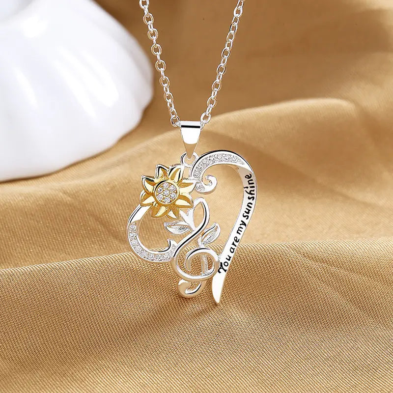 Silver and gold heart-shaped pendant necklace with sunflower design, embedded crystals along the heart edges, and engraved text reading you are my sunshine.