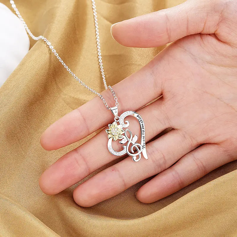 Silver heart-shaped pendant necklace featuring a gold-toned sunflower and musical note design with engraved text along the curve from the You Are My Sunshine collection.
