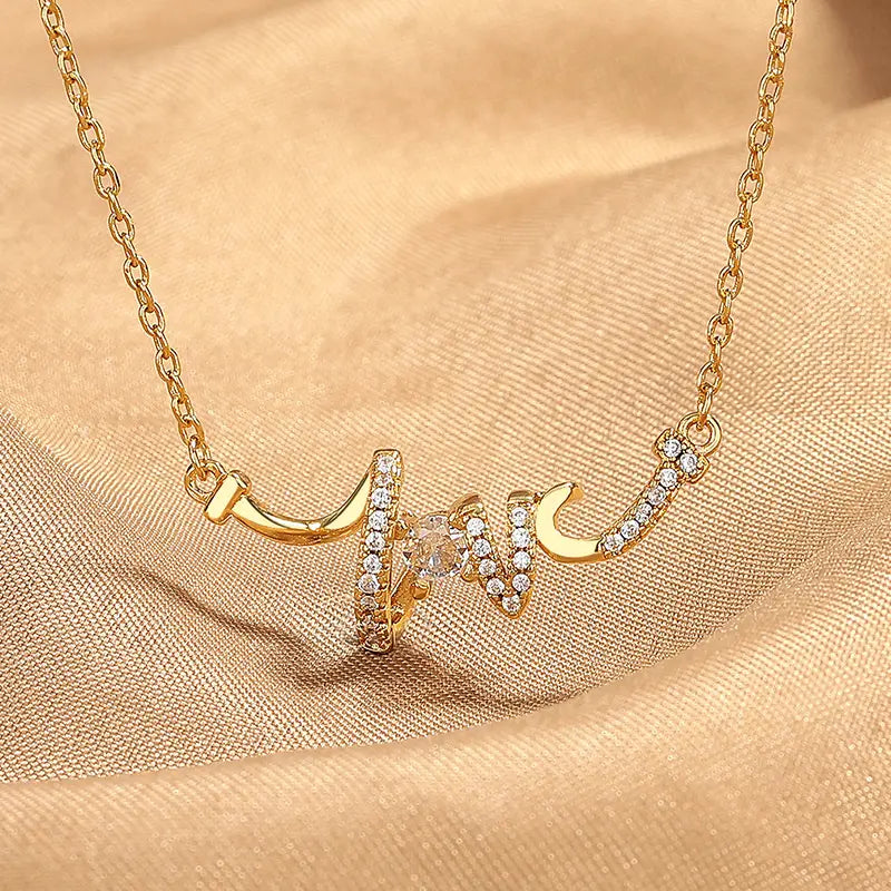 Elegant cursive love pendant necklace in gold and silver featuring a gold-toned necklace with a heart-shaped pendant adorned with clear crystals and an intricate flowing design.
