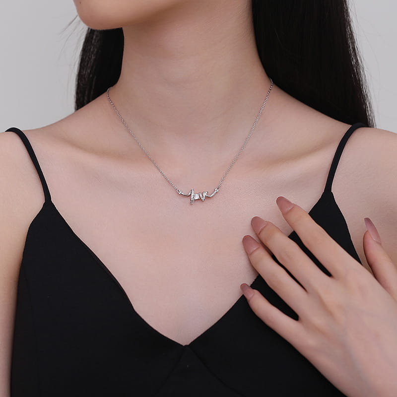 A delicate silver necklace featuring an elegant cursive love pendant adorned with small sparkling stones worn gracefully against the skin.