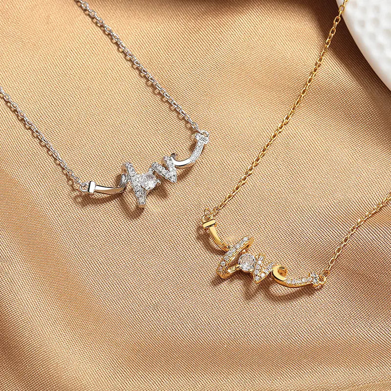 Two elegant cursive love pendant necklaces in silver and gold metals adorned with sparkling clear stones along the delicate script lettering.