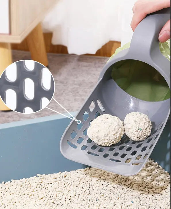 Gray plastic cat litter scoop with perforated design and handle holding two clumped white pellets featuring an integrated bag dispenser for convenient use.