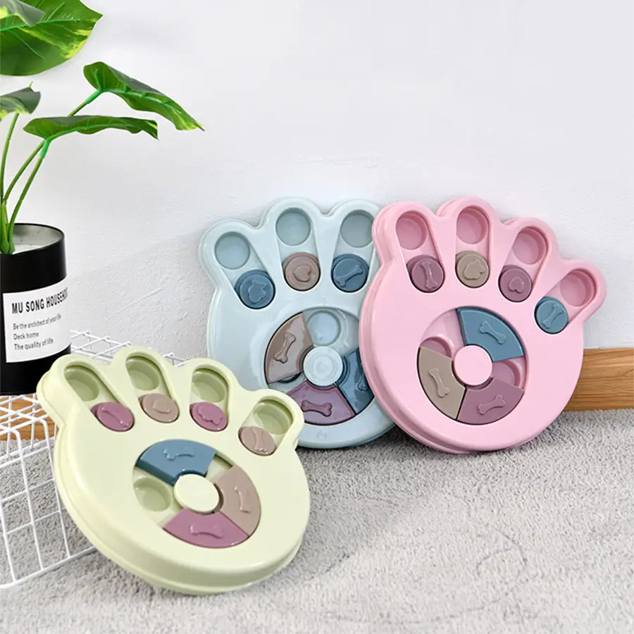 Pastel-colored plastic paw-shaped dog puzzle toy features segmented compartments and bone-patterned puzzle pieces for interactive slow feeder training games.