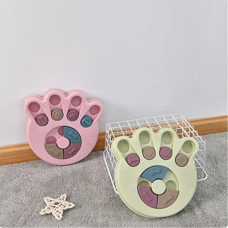 Pink and cream-colored paw-shaped dog puzzle toy with colorful bone-patterned compartments designed for interactive slow feeder training games.