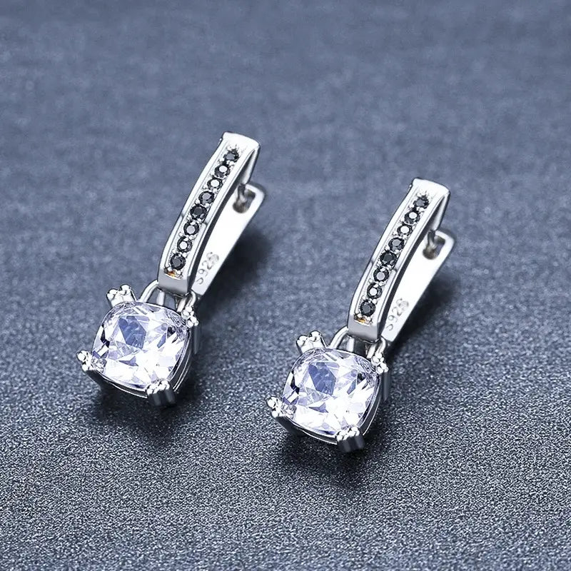 Boucles d’oreilles huggie en argent présentant une pierre centrale en oxyde de zirconium cubique transparent, entourée de petites pierres noires, le long d’une monture métallique incurvée, dans un design de boucles d’oreilles pendantes en argent avec zircon carré et diamant noir.