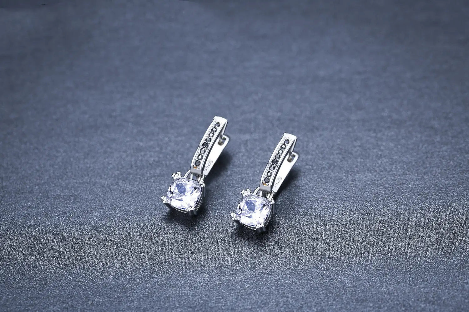Boucles d’oreilles créoles en argent avec une gemme en zircon transparent à facettes carrées au centre et une rangée de petits diamants noirs le long de la monture incurvée en argent.