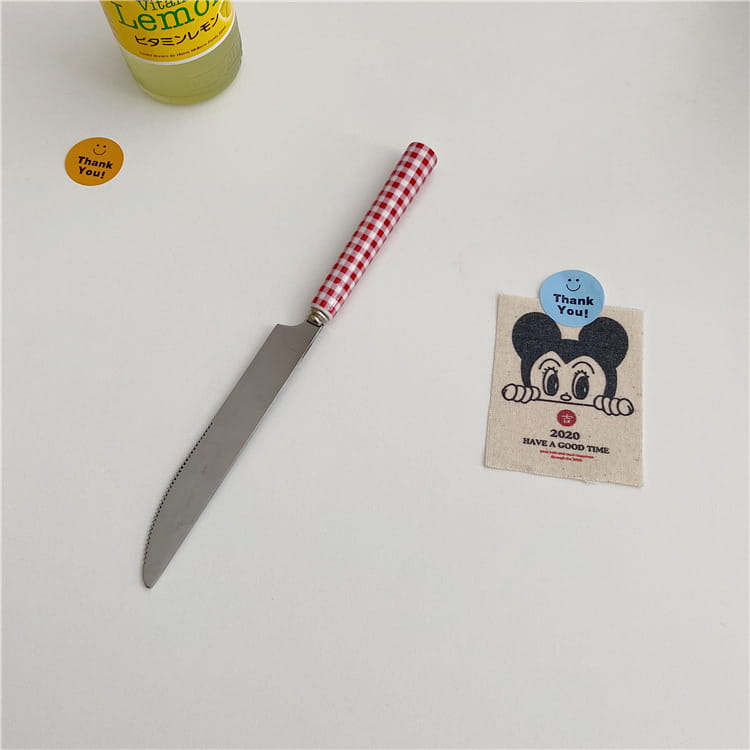 A red and white checkered handle serrated knife with a stainless steel blade from the checkered stainless steel cutlery tableware set.