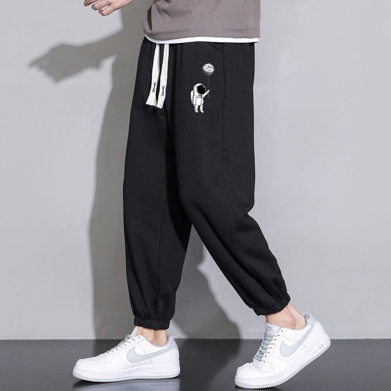 Men astronaut graphic joggers casual pants featuring black cotton fabric with white drawstrings and an astronaut graphic on the thigh.