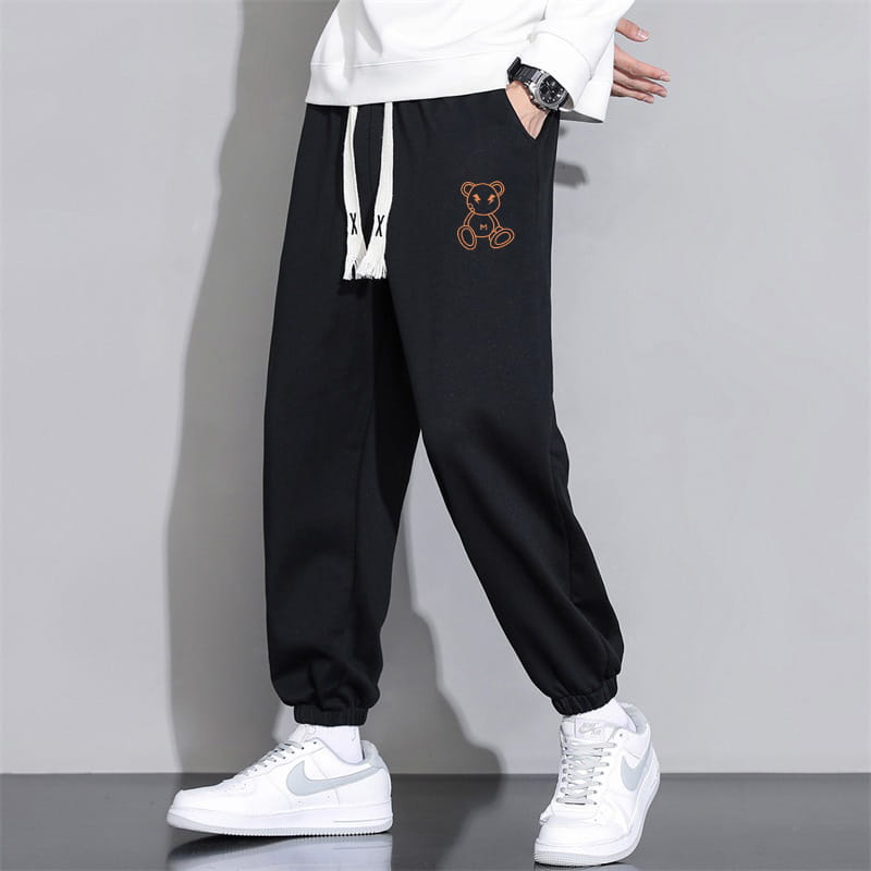Men astronaut graphic joggers in black cotton featuring white drawstrings and an embroidered orange bear on the thigh for casual wear.