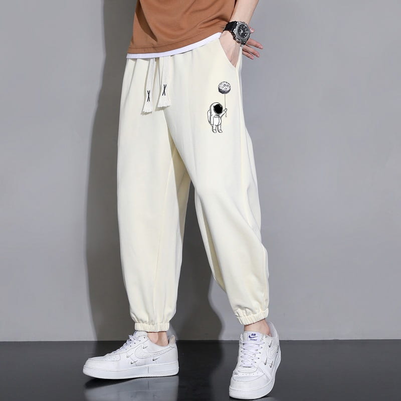 Men astronaut graphic joggers in cream-colored cotton featuring a playful astronaut graphic on the thigh and matching drawstring ties for casual wear.