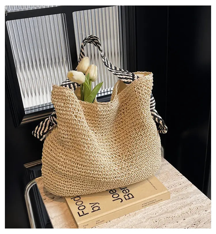 beige woven straw tote bag with black and white striped bow handles for stylish carrying.