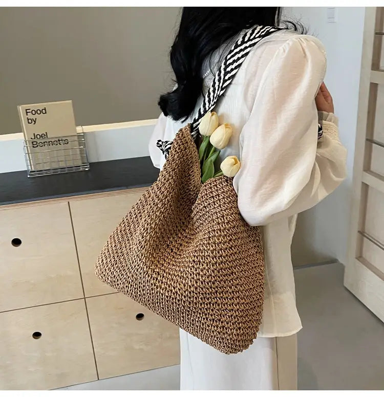 A beige woven straw tote bag with a textured crochet pattern and black and white striped shoulder straps designed for stylish carrying.