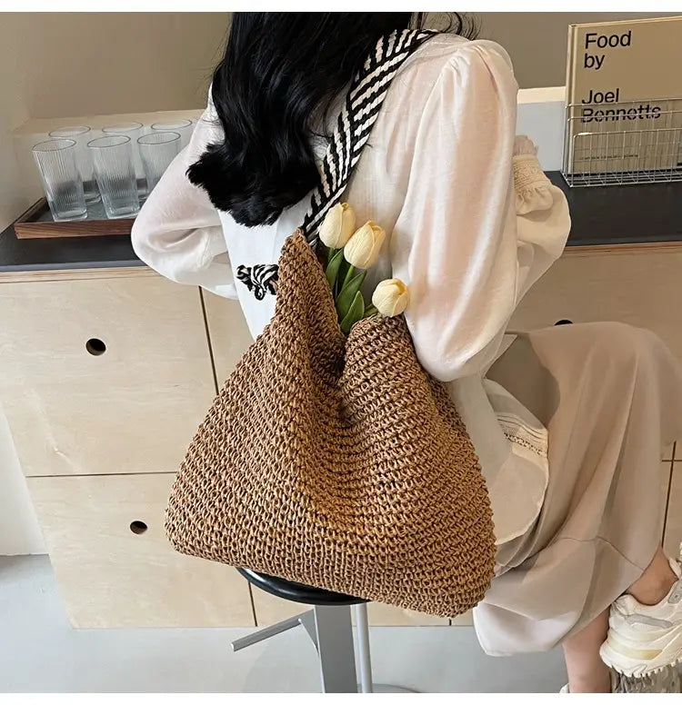 Beige woven straw tote bag with black and white striped shoulder strap featuring bow handles.