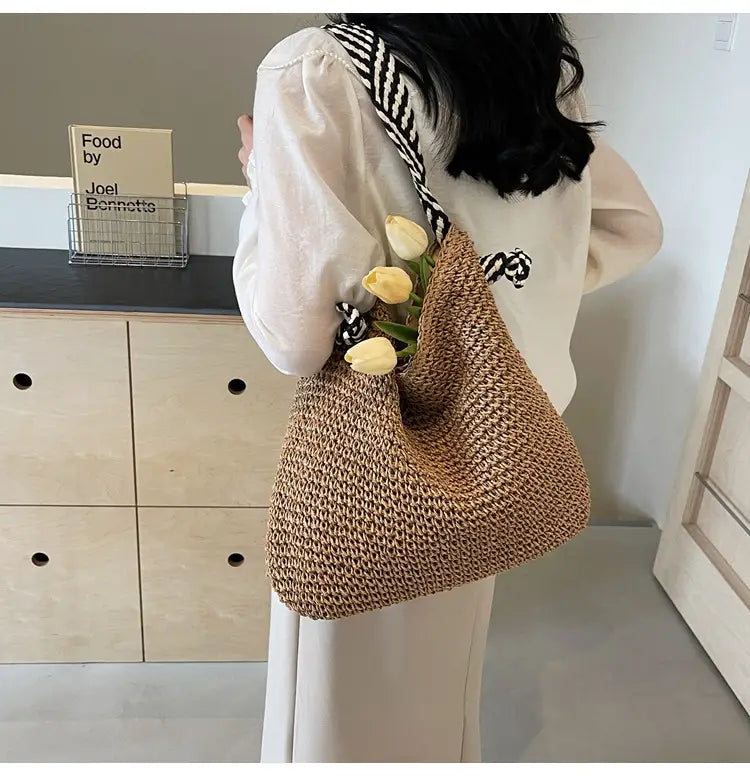 Beige woven straw tote bag with black and white striped bow handles adorned with fresh yellow tulips.