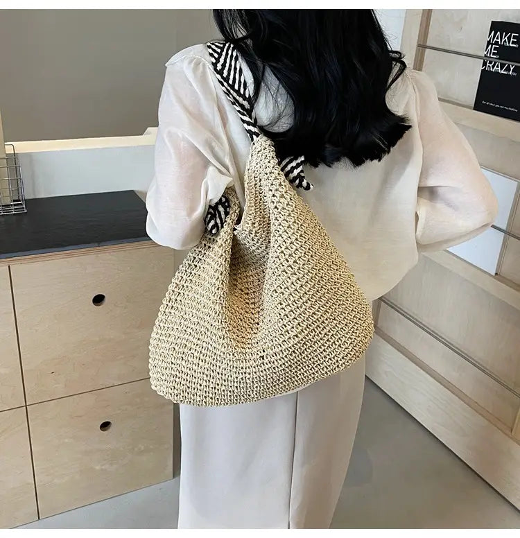 Beige woven straw tote bag with black and white striped shoulder strap and bow handles suitable for casual use.