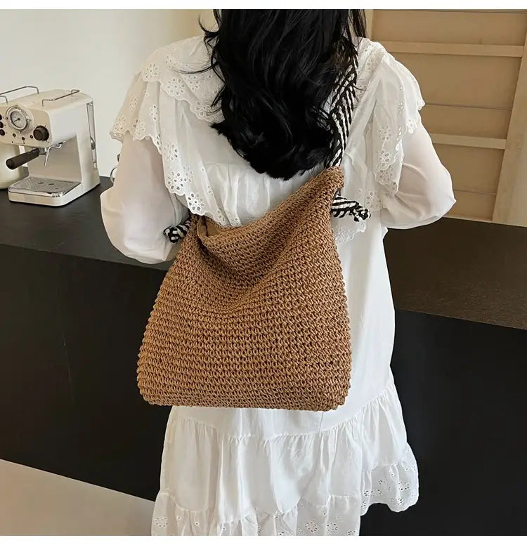 A tan hand-crocheted straw tote bag with soft textured weave and striped bow handles in a slouchy silhouette.