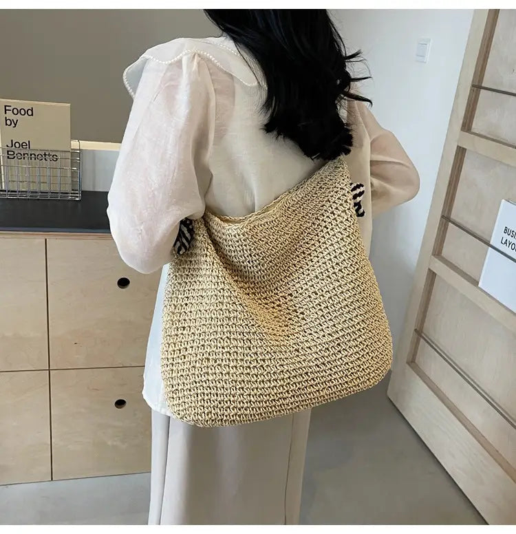 Beige woven straw tote bag with a soft textured crochet pattern and striped bow handles featuring a relaxed slouchy silhouette.