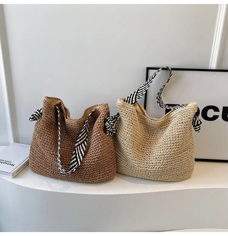 two woven straw tote bags in warm tan and natural beige featuring contrasting black and white striped fabric handles tied into decorative bows