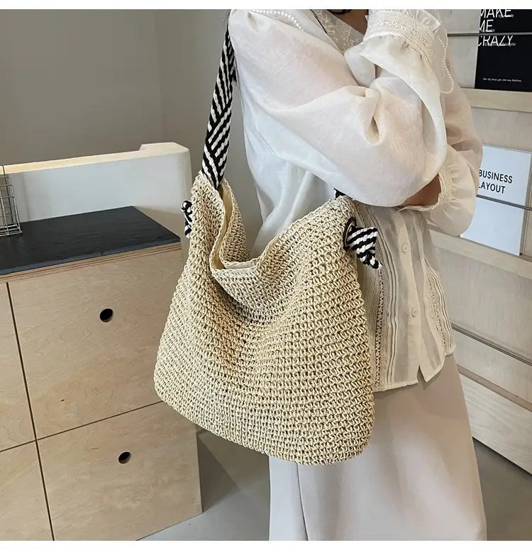 Beige woven straw tote bag with black and white striped shoulder strap featuring striped bow handles for versatile casual use.