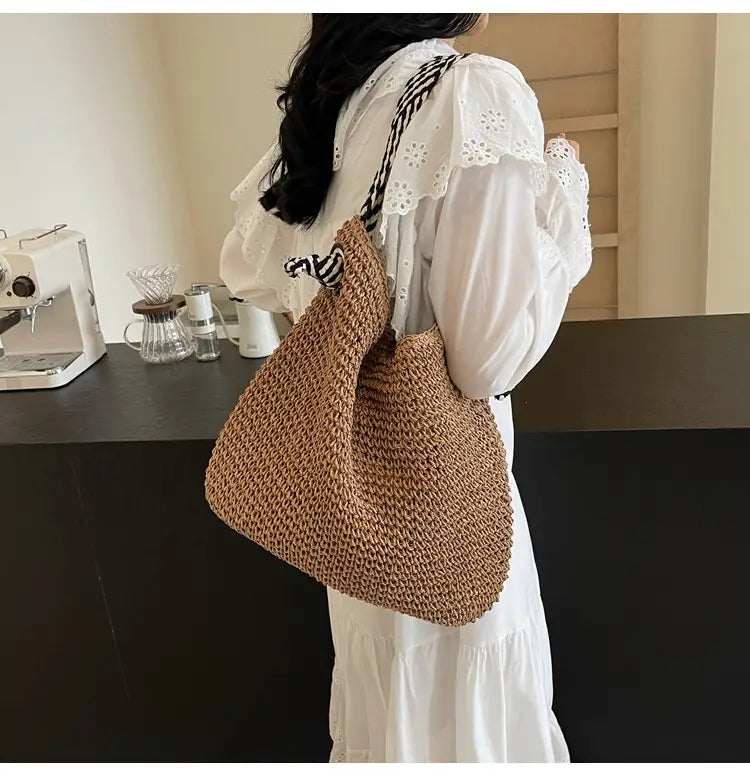 Beige woven straw tote bag with black and white striped shoulder strap featuring bow handles.