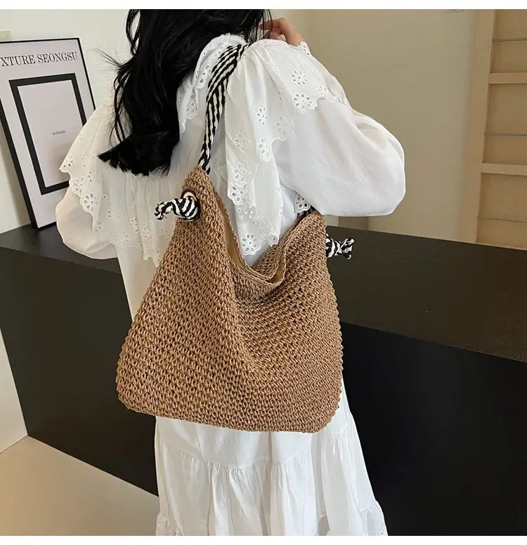 Beige woven straw tote bag with black and white striped rope handles tied in decorative knots featuring striped bow handles.