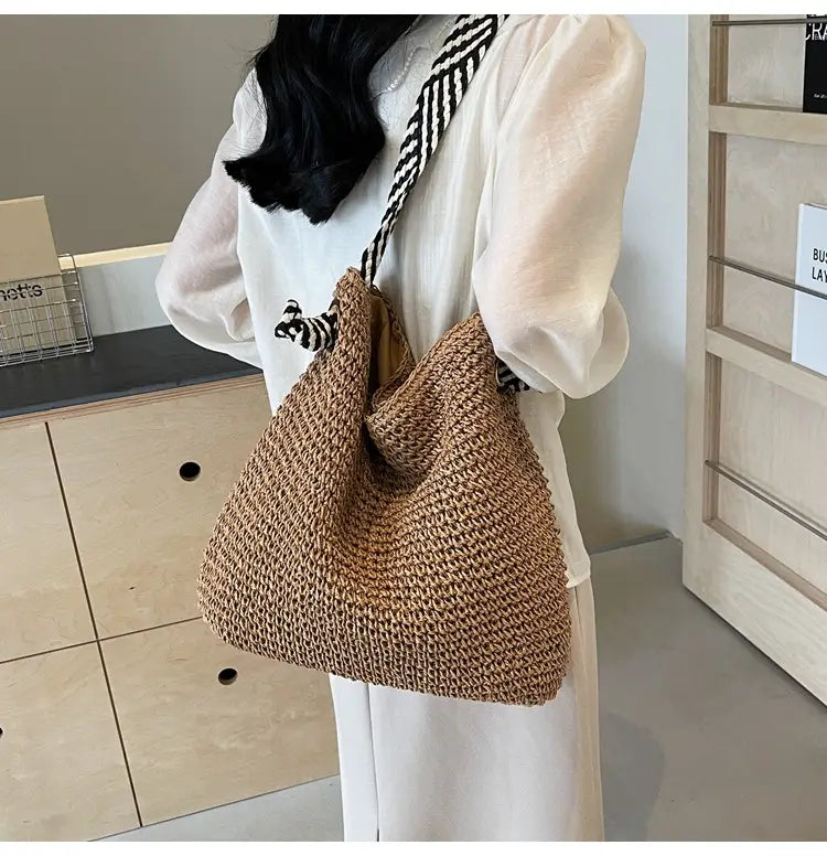 Beige woven straw tote bag with black and white striped shoulder strap featuring striped bow handles.