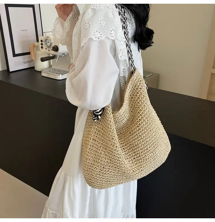 Beige woven straw tote bag with striped black and white bow handles designed as a hobo style accessory.