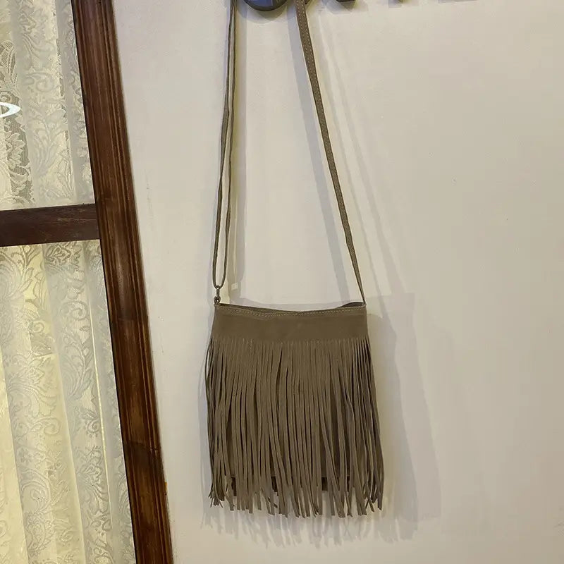 A taupe suede fringe crossbody bag with a long adjustable strap designed as an artistic tassel canvas shoulder bag for travel.